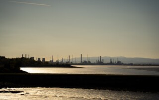 Oil refinery complex across a waterfront under an overcast sky